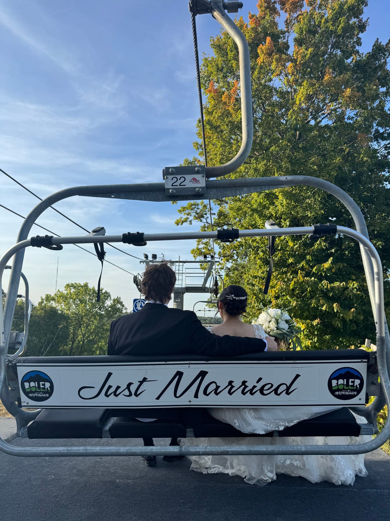 Chai and Jared riding a ski chairlift with a Just Married sign