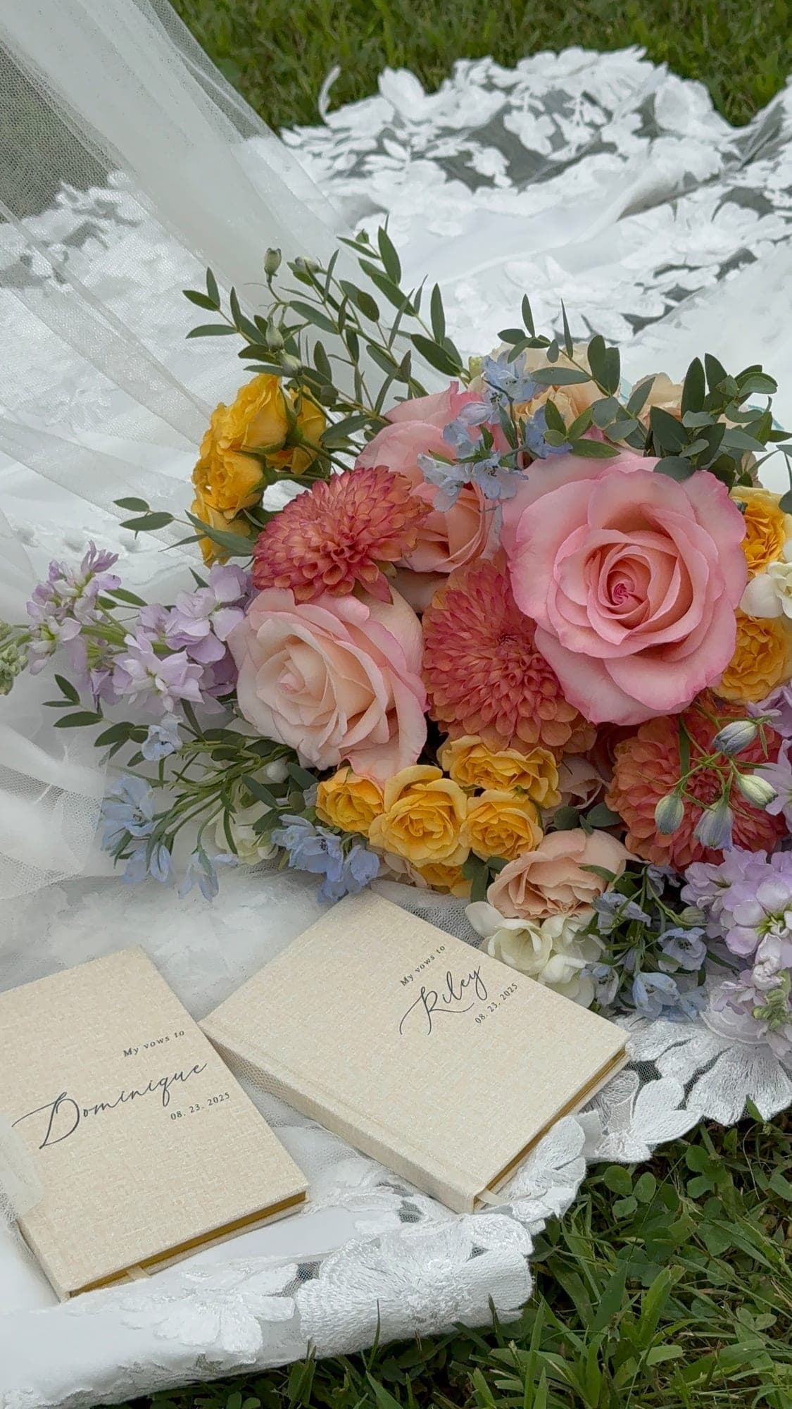 Two handwritten vow books resting beside a bright bouquet on the bride's train